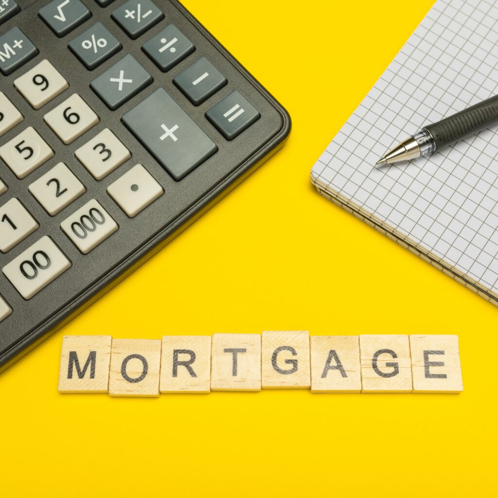 Word mortgage made with wood letters on yellow background and modern calculator with pen and notebook. Copy space. Economy, money planning. Business, finance concept. Tax burden. Taxes and taxation.