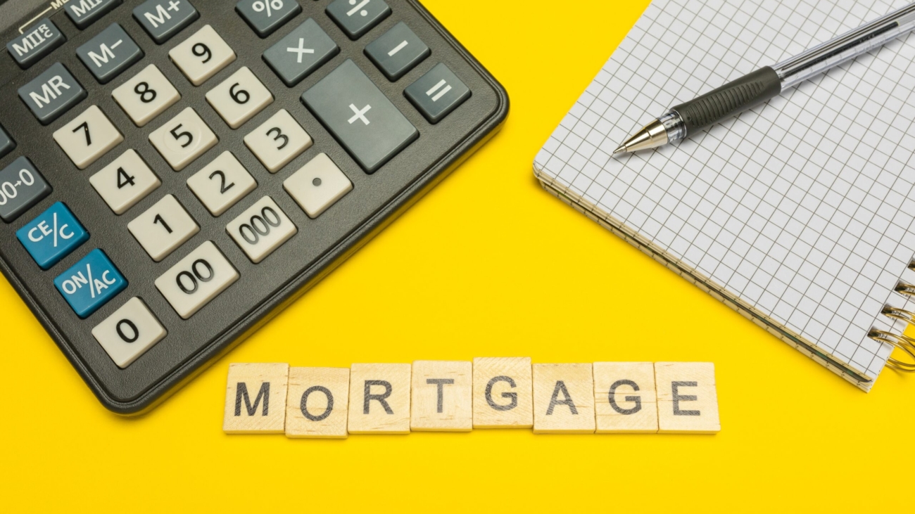 Word mortgage made with wood letters on yellow background and modern calculator with pen and notebook. Copy space. Economy, money planning. Business, finance concept. Tax burden. Taxes and taxation.
